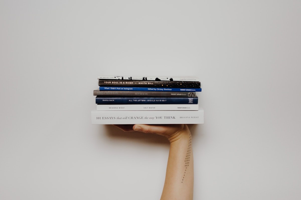 Une main portant une pile de livres devant un mur clair.